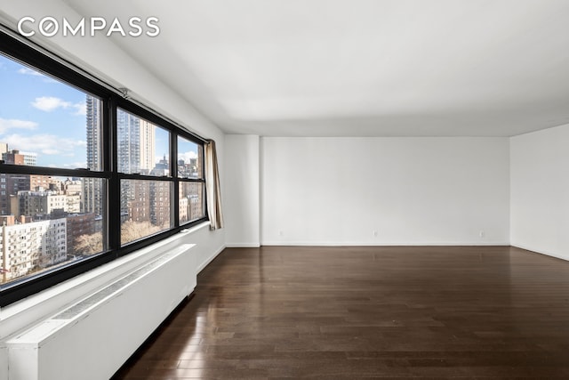 unfurnished room featuring baseboards, radiator heating unit, dark wood-style flooring, and a city view