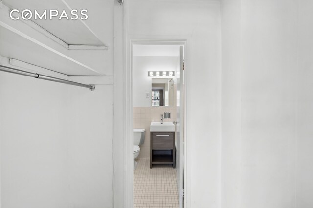 bathroom featuring toilet, a wainscoted wall, vanity, tile walls, and tile patterned floors