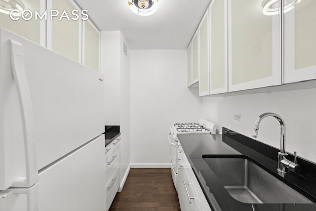 kitchen with dark countertops, white appliances, white cabinetry, and a sink