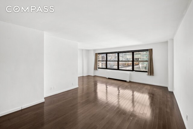 unfurnished room with radiator, dark wood-style floors, and baseboards