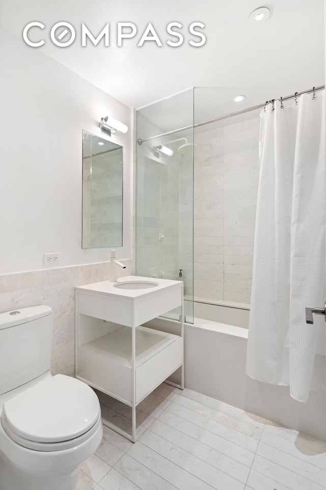 bathroom featuring vanity, shower / bathtub combination with curtain, wainscoting, tile walls, and toilet