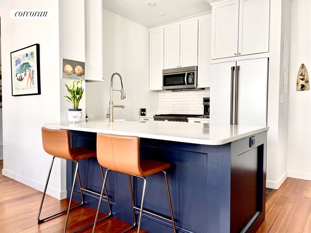 kitchen featuring stainless steel microwave, a breakfast bar, baseboards, light wood-type flooring, and backsplash