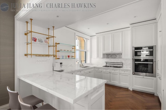 kitchen featuring a breakfast bar, dark parquet floors, white cabinetry, kitchen peninsula, and light stone countertops