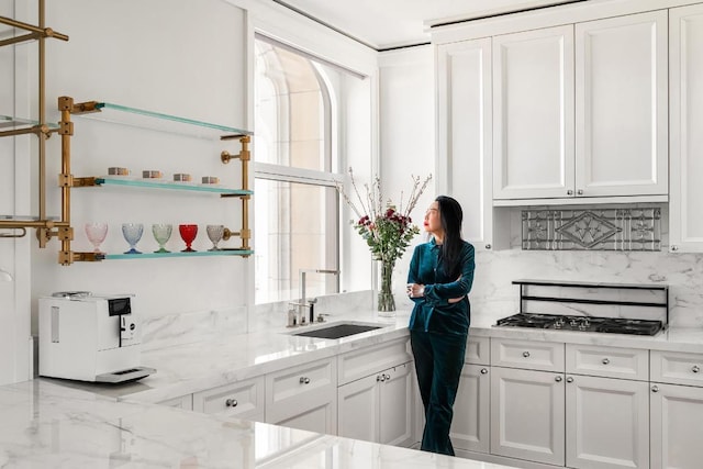 kitchen with sink, light stone counters, white cabinetry, tasteful backsplash, and stainless steel gas stovetop