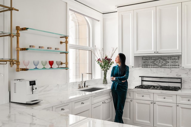 kitchen with light stone countertops, gas cooktop, open shelves, a sink, and white cabinetry
