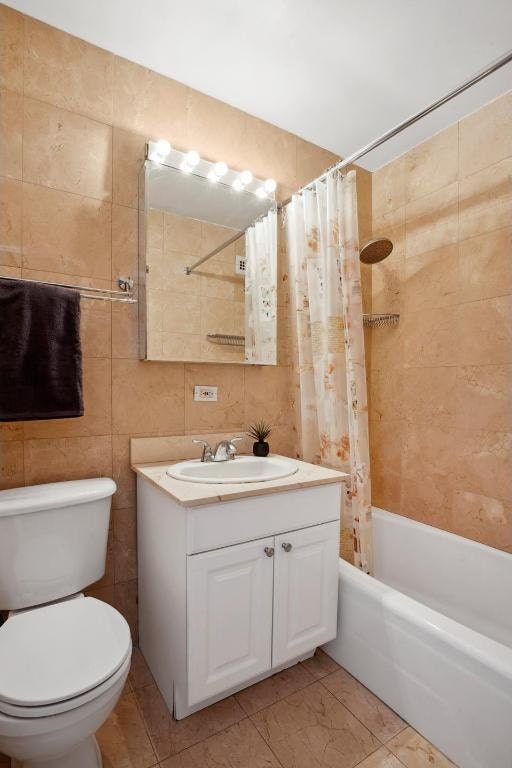 full bathroom with shower / bath combo with shower curtain, vanity, toilet, and tile walls