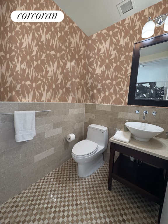 bathroom with toilet, sink, and tile walls