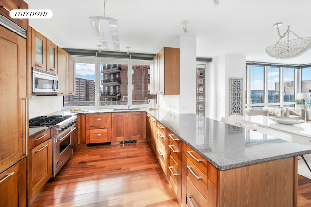 kitchen featuring hanging light fixtures, kitchen peninsula, hardwood / wood-style flooring, stainless steel appliances, and light stone countertops