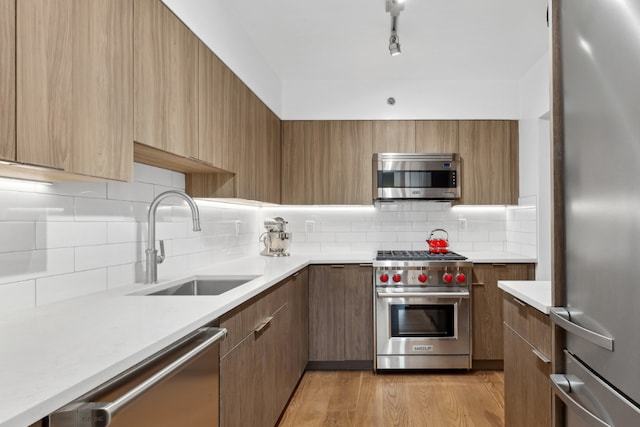 kitchen with a sink, light countertops, appliances with stainless steel finishes, brown cabinetry, and modern cabinets