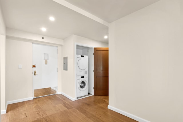 hallway with baseboards, electric panel, light wood-style flooring, and stacked washing maching and dryer