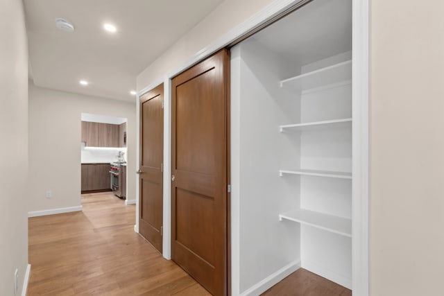 corridor featuring baseboards, recessed lighting, and light wood-style floors