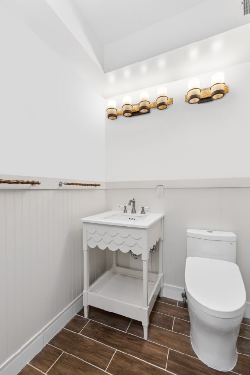 half bath featuring a wainscoted wall, a sink, toilet, and wood tiled floor