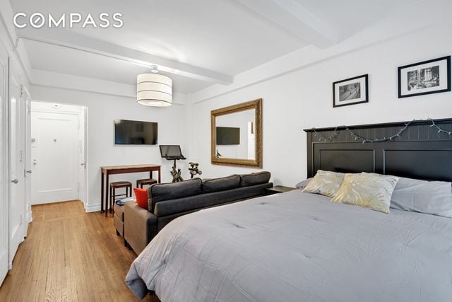 bedroom featuring beamed ceiling and light wood-type flooring