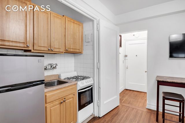 kitchen featuring stainless steel fridge, backsplash, light hardwood / wood-style floors, white range with gas cooktop, and light brown cabinets