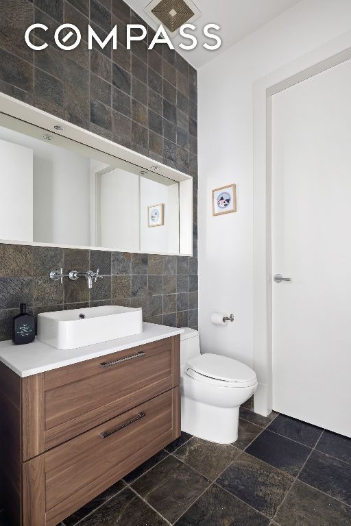 bathroom with vanity, tile walls, decorative backsplash, and toilet