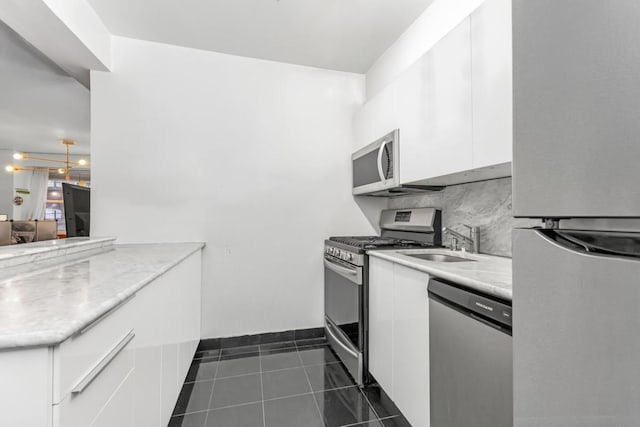 kitchen with sink, dark tile patterned flooring, stainless steel appliances, decorative backsplash, and white cabinets