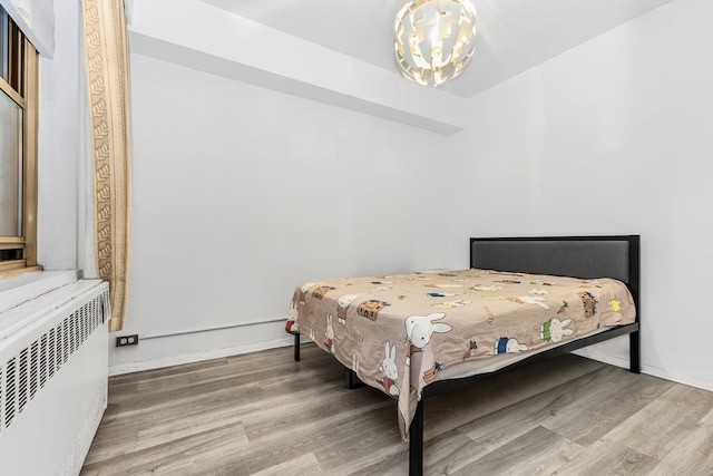 bedroom featuring a notable chandelier, baseboards, wood finished floors, and radiator