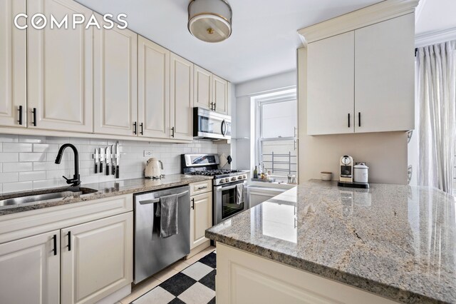 kitchen featuring light stone counters, sink, decorative backsplash, and appliances with stainless steel finishes