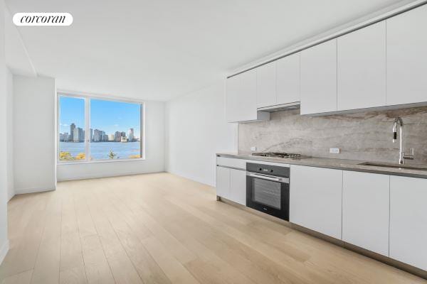 kitchen with white cabinetry, sink, oven, stainless steel gas cooktop, and light hardwood / wood-style flooring