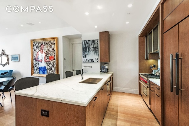 kitchen featuring sink, light hardwood / wood-style flooring, a kitchen island with sink, high end appliances, and light stone countertops