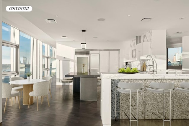 kitchen featuring a breakfast bar area, visible vents, white cabinets, light countertops, and dark wood-style floors