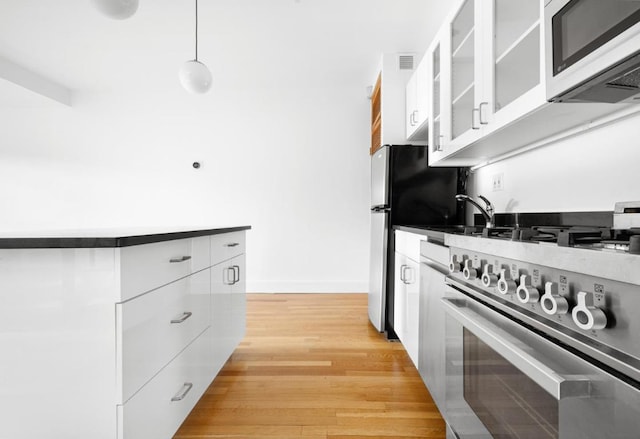 kitchen featuring decorative light fixtures, stainless steel appliances, white cabinets, and light wood-type flooring