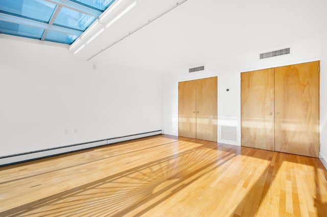 unfurnished bedroom with multiple closets, a baseboard radiator, wood-type flooring, and a skylight