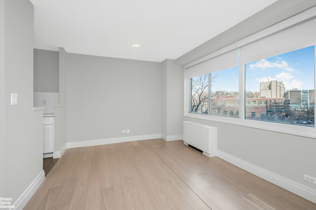 unfurnished room featuring radiator, light wood-style flooring, and baseboards