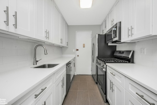 kitchen with sink, white cabinetry, dark tile patterned flooring, stainless steel appliances, and tasteful backsplash