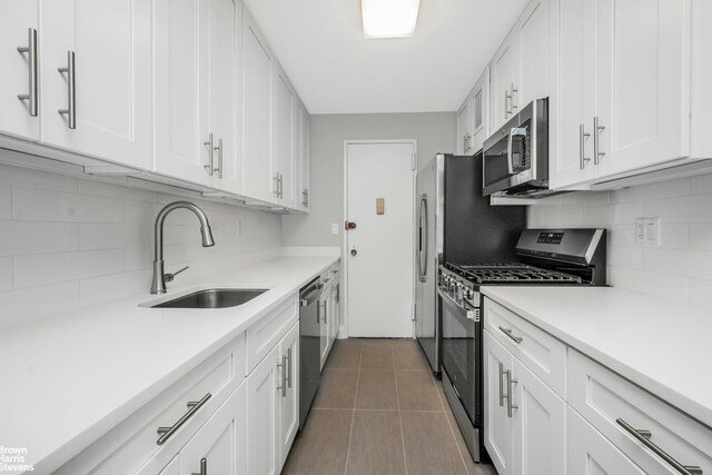 kitchen with light countertops, appliances with stainless steel finishes, white cabinets, a sink, and tile patterned flooring