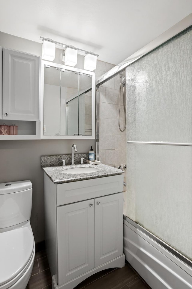 bathroom with toilet, wood tiled floor, enclosed tub / shower combo, and vanity