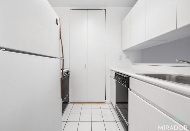 kitchen with black dishwasher, freestanding refrigerator, light countertops, white cabinetry, and a sink