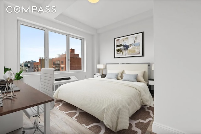 bedroom with a view of city, light wood finished floors, and baseboards