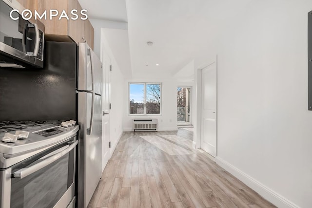 kitchen with appliances with stainless steel finishes, heating unit, and light hardwood / wood-style flooring