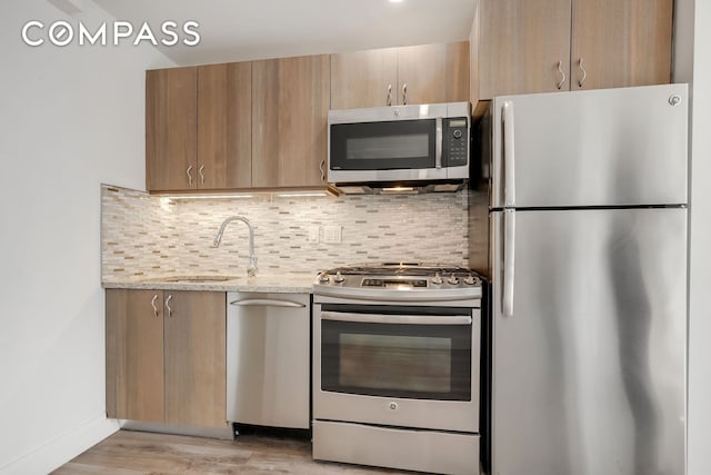 kitchen featuring light stone countertops, light wood-style flooring, a sink, stainless steel appliances, and tasteful backsplash