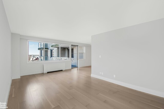 unfurnished living room featuring radiator, light wood-style floors, and baseboards