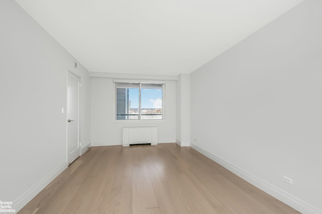 unfurnished room featuring light wood-type flooring, radiator heating unit, and baseboards