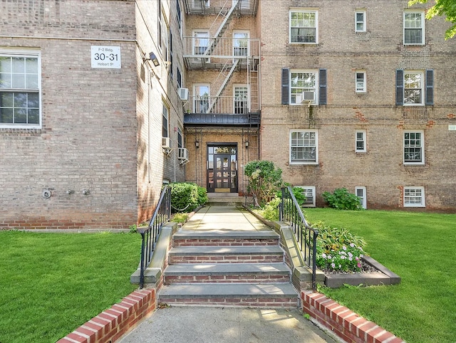 view of exterior entry with cooling unit, brick siding, and a yard