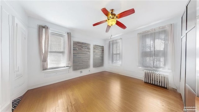 spare room with wood finished floors, visible vents, baseboards, a ceiling fan, and radiator