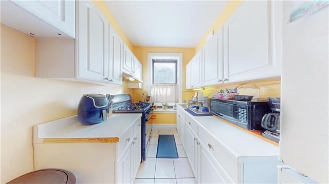 kitchen featuring light tile patterned floors, white cabinetry, range with gas stovetop, light countertops, and stainless steel microwave