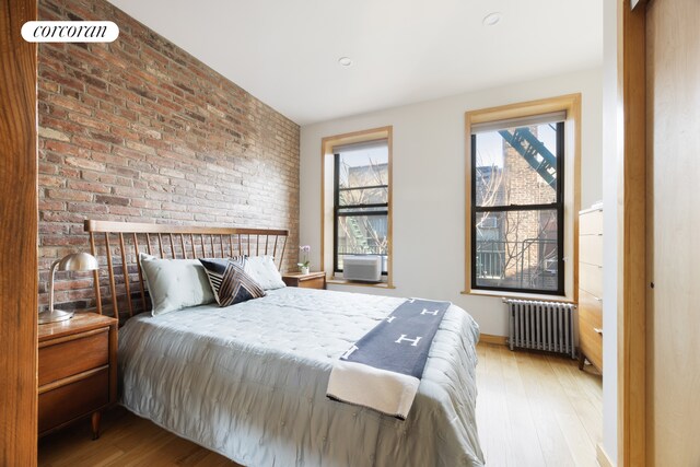 bedroom featuring radiator, hardwood / wood-style floors, and brick wall