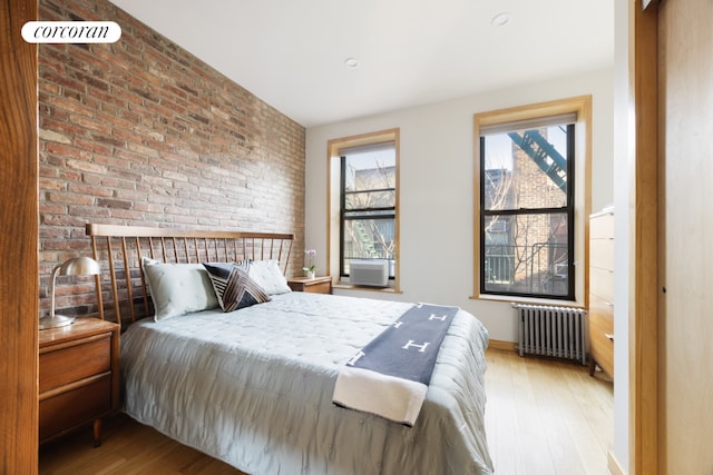 bedroom with radiator, hardwood / wood-style flooring, and brick wall