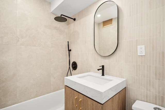 full bathroom featuring tiled shower / bath, vanity, toilet, and tile walls