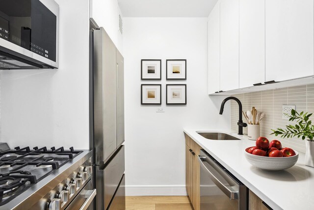 kitchen featuring appliances with stainless steel finishes, tasteful backsplash, white cabinetry, sink, and light hardwood / wood-style flooring