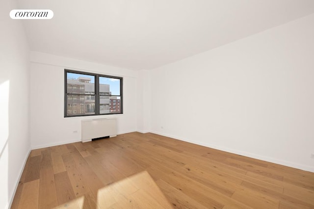 unfurnished room featuring baseboards, wood finished floors, visible vents, and radiator