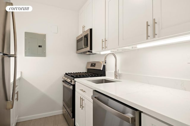 kitchen with electric panel, white cabinetry, stainless steel appliances, and a sink