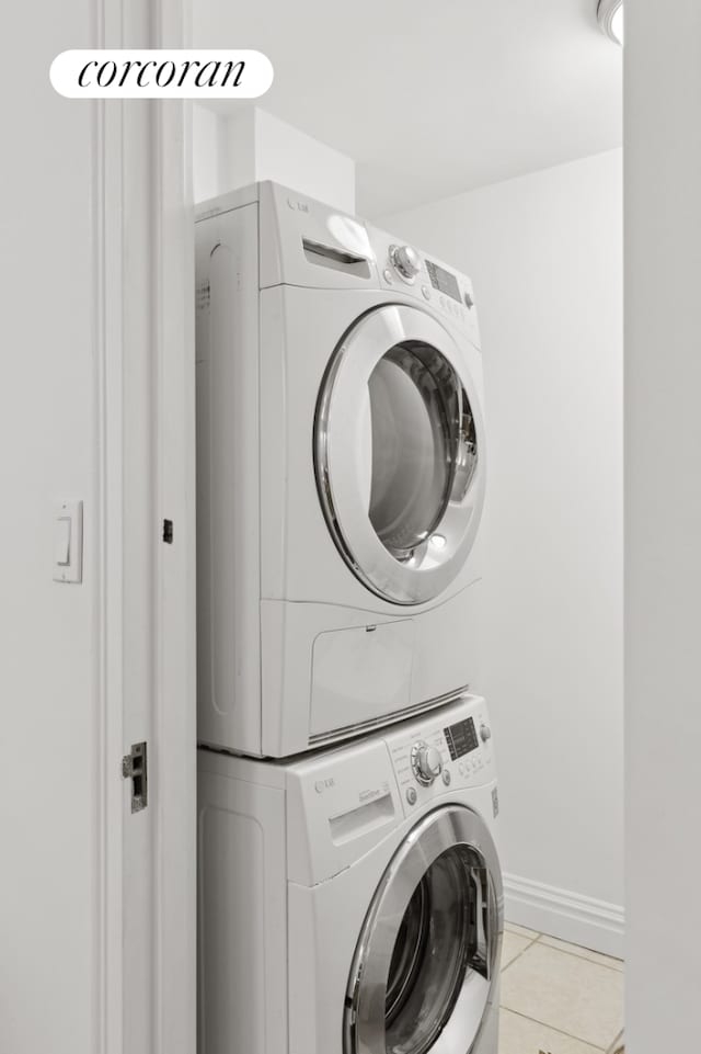 laundry room with laundry area, stacked washer / dryer, light tile patterned floors, and baseboards