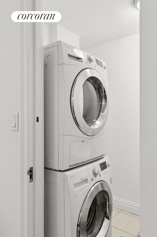 washroom featuring light tile patterned floors, laundry area, stacked washer / drying machine, and baseboards