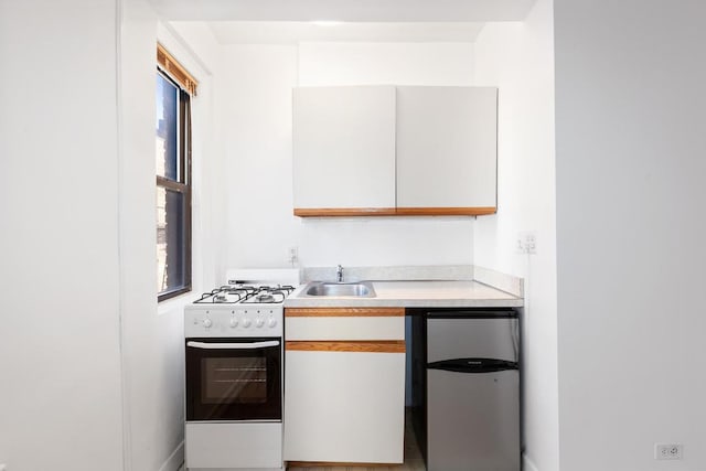 kitchen featuring stainless steel refrigerator, sink, white range with gas stovetop, and white cabinets