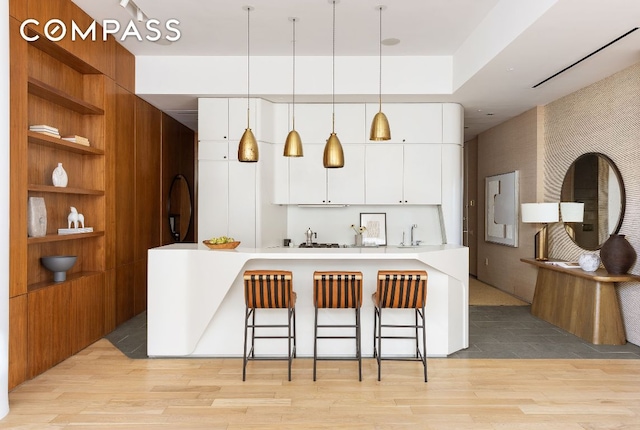 kitchen with hanging light fixtures, light hardwood / wood-style flooring, sink, and white cabinets